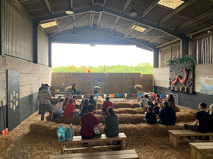 A diverse group of people sitting on hay bales in a barn at the Discovery Barn, a versatile space for food and farming events.
