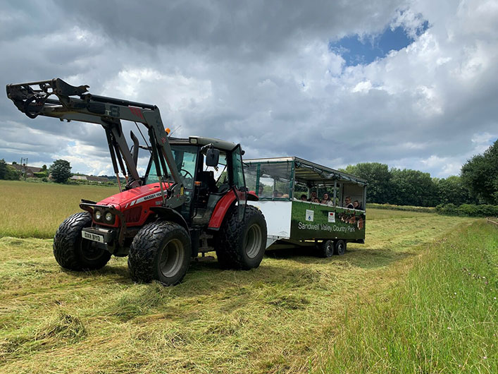 A tractor pulling a trailer through a field during a farm tour, showcasing seasonal interactions and demonstrations.