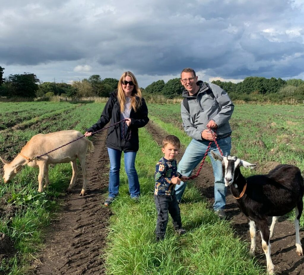 A man, woman, and child interact with two goats in a field during a farmer for the day experience.